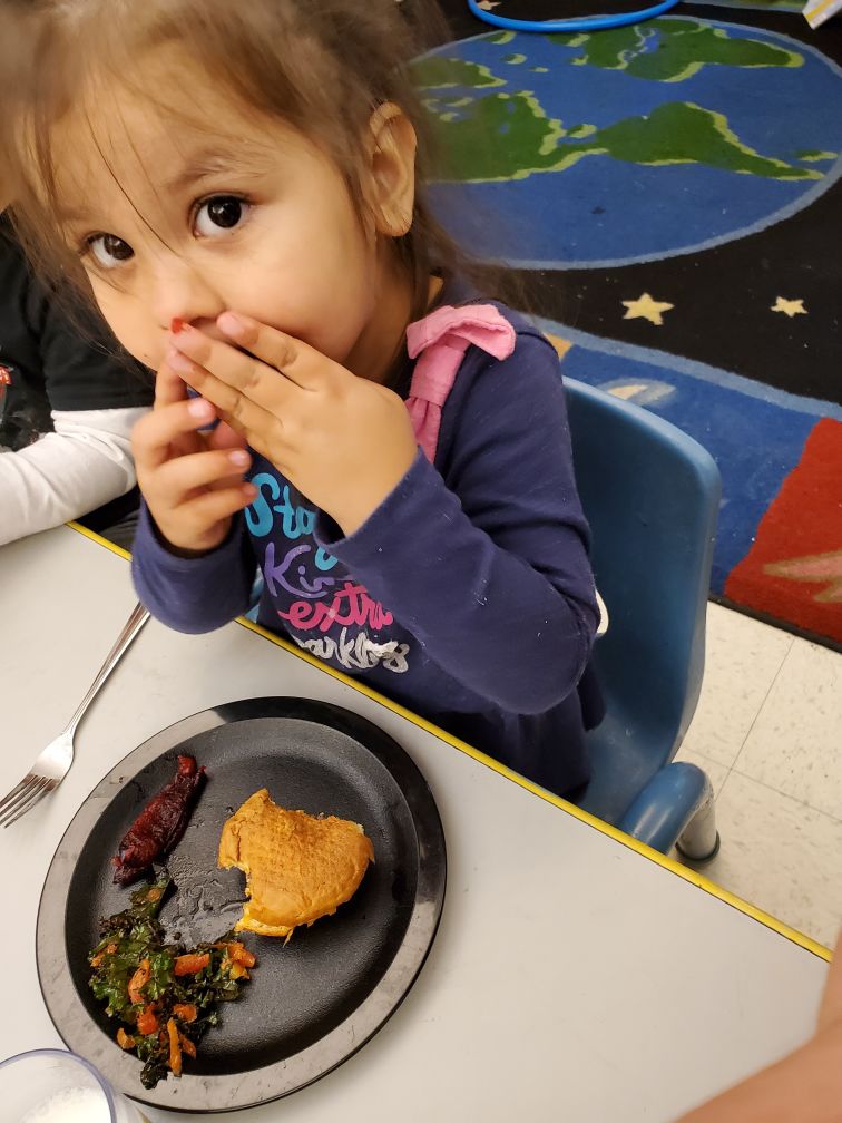 Photo of a girl eating a meal on a black plate, looking at the camera.